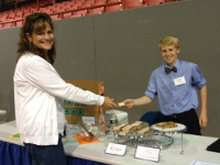 Photo of young entrepreneur giving his granola bar to a woman in front of his stand.
