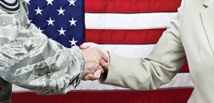 Soldier and businessperson shaking hands in front of American flag