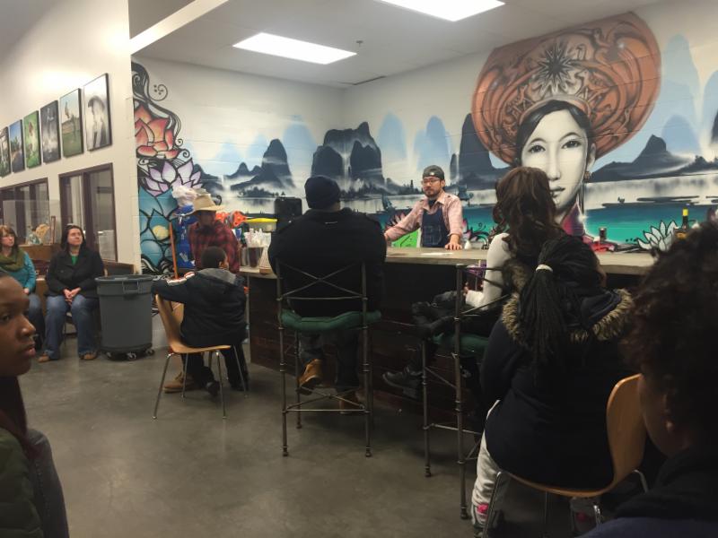 Photo of man standing behind a bar with murals on teh wall behind him